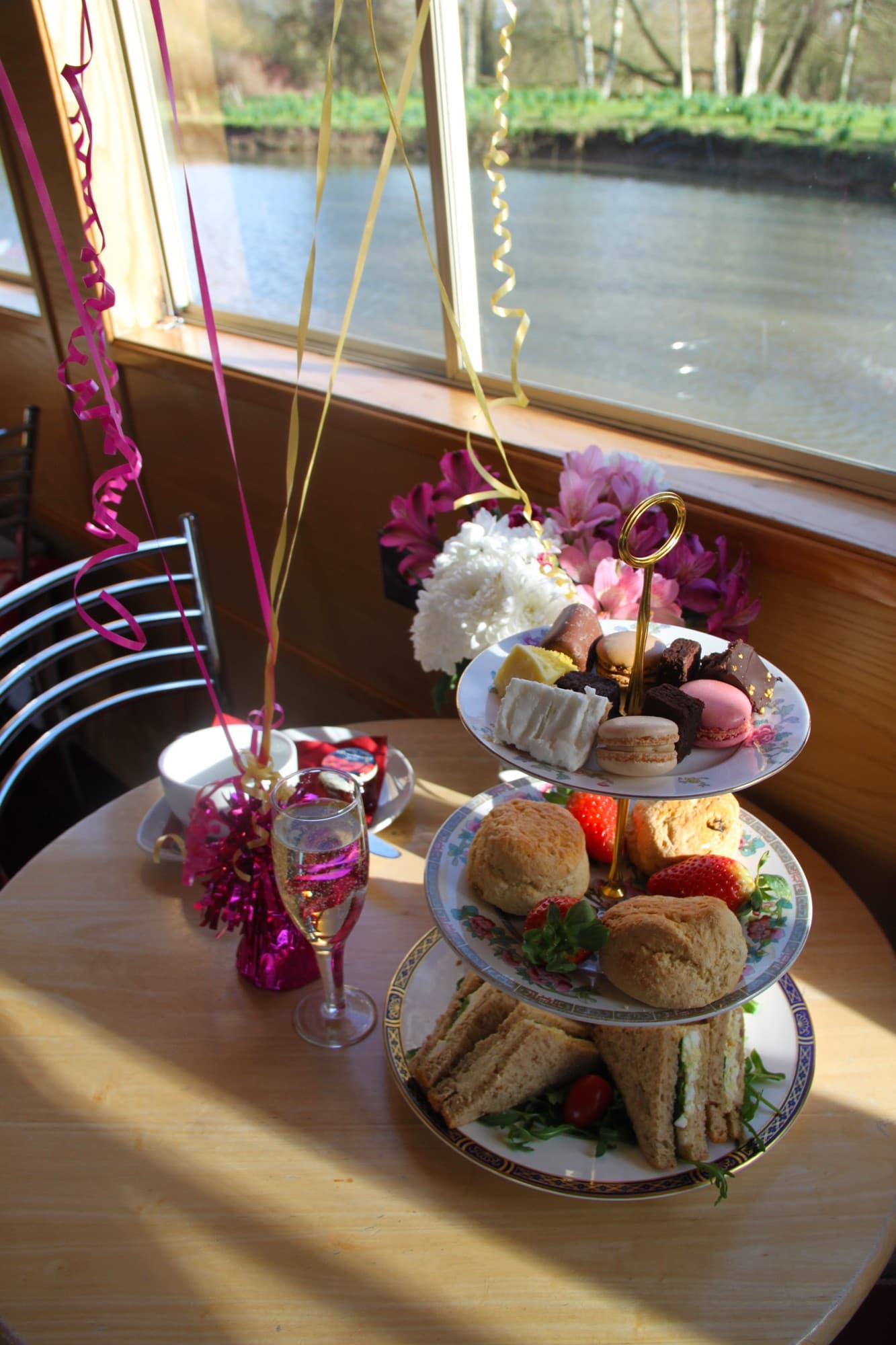 A tiered afternoon tea of sandwiches, scones and cakes with Prosecco, beside the river window onboard